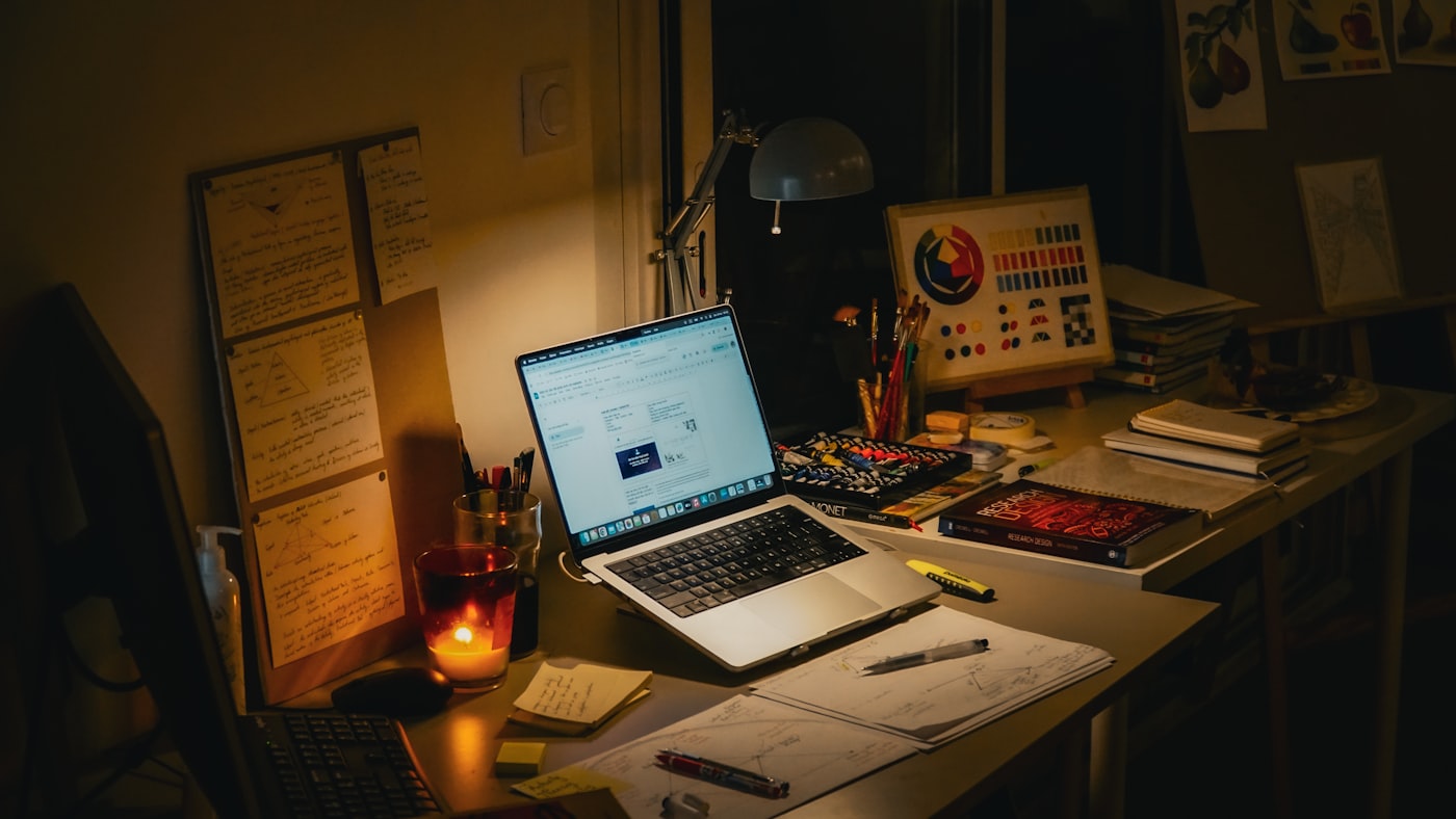 A desk at night with notes, a laptop and a candle